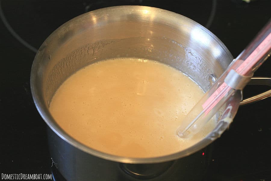 A saucepan full of the ingredients to make sweetened consdensed milk marshmallows, with a candy thermometer clipped to the side.