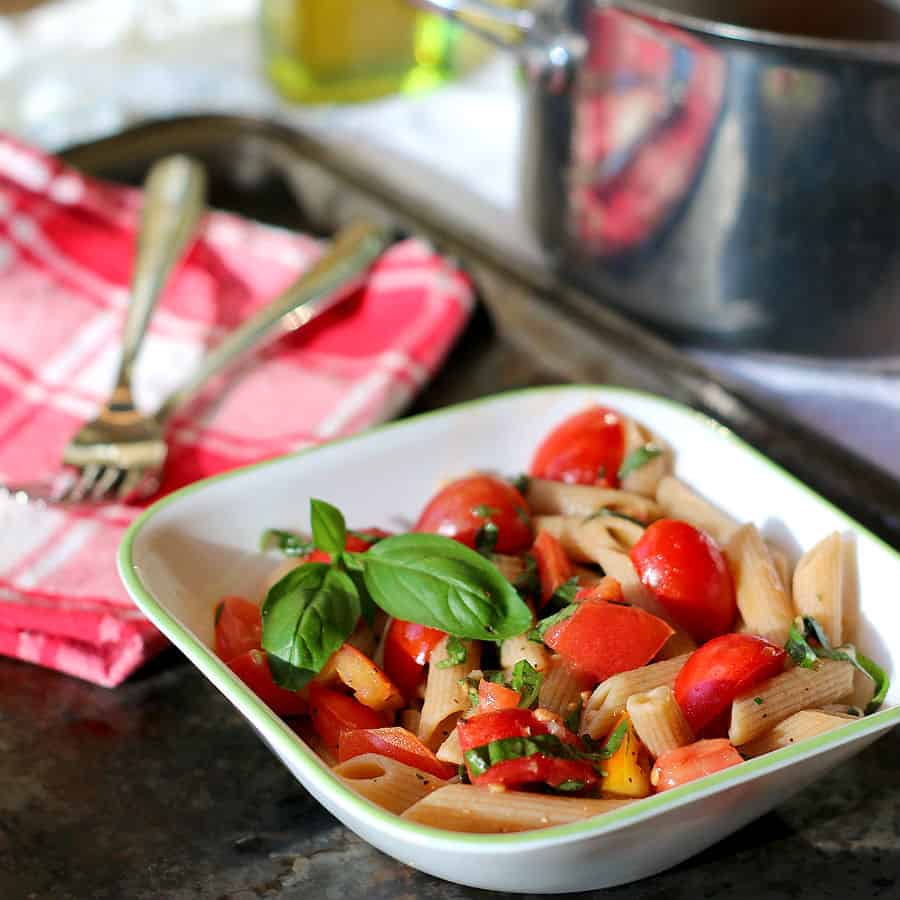 Whole wheat pasta with fresh tomatoes and herbs in a white bowl.