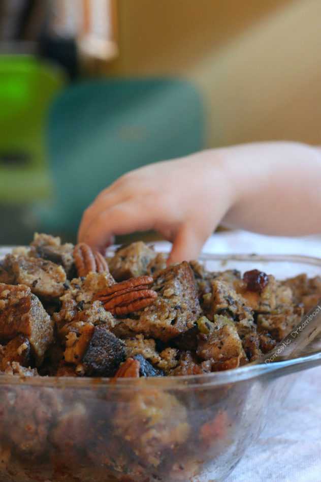 A child's hand grabbing stuffing from a baking dish.