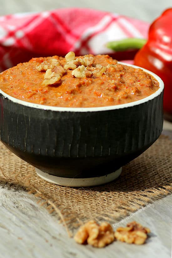 Roasted red pepper dip garnished with chopped walnuts in a black bowl.