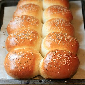 Homemade hamburger buns on a baking sheet.