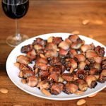 Bacon-Wrapped Stuffed Dates on a white plate with a glass of wine.
