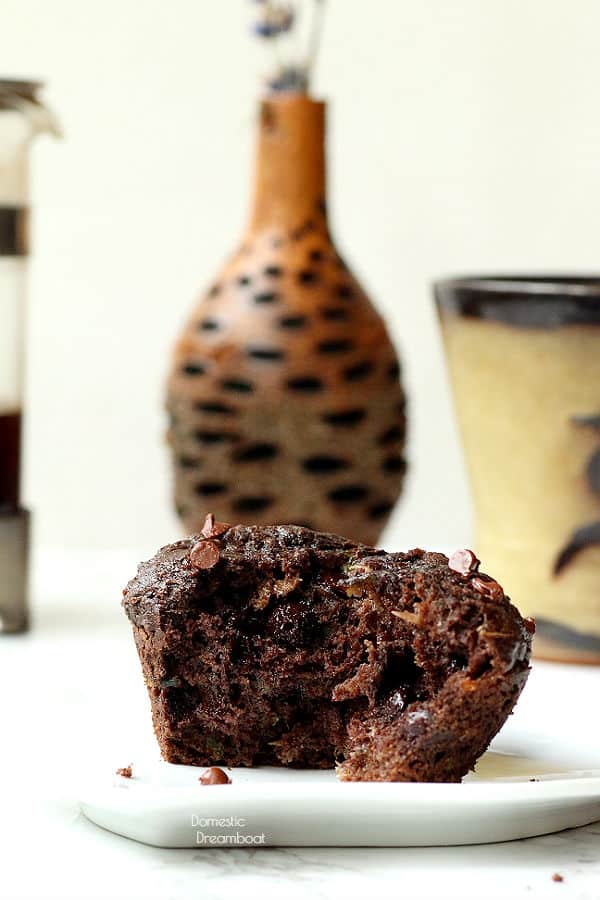 Double chocolate zucchini muffin broken in half with flower vase and coffee cup
