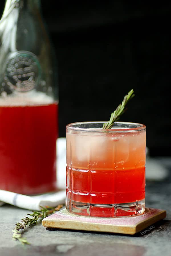 Strawberry shrub in a glass with a bottle of shrub syrup in the background.