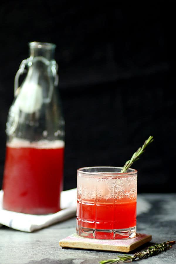 Strawberry shrub in a glass with a bottle of shrub syrup in the background.