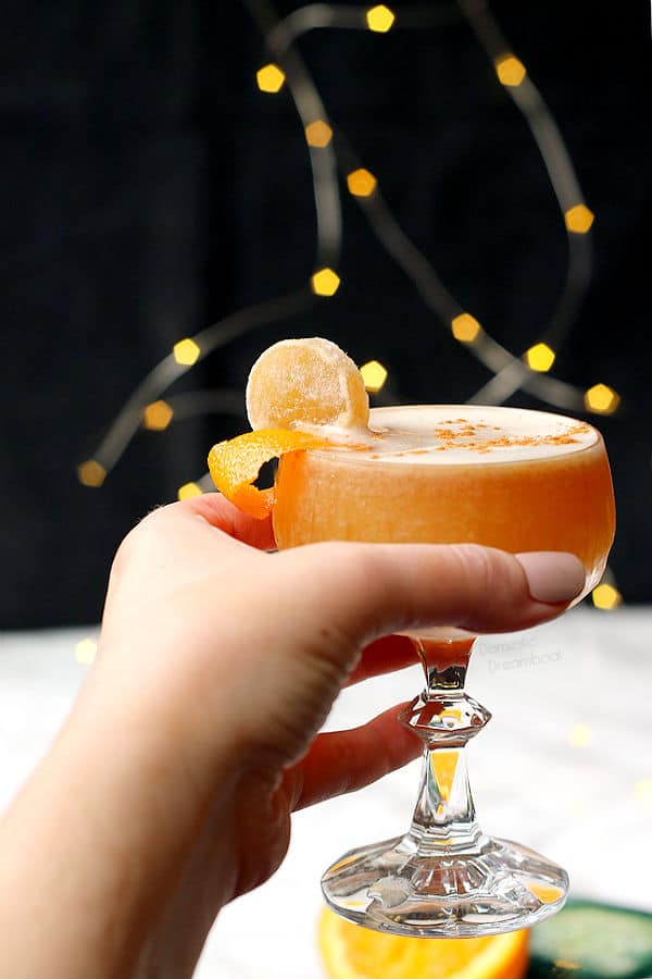A hand holding an orange whisky sour