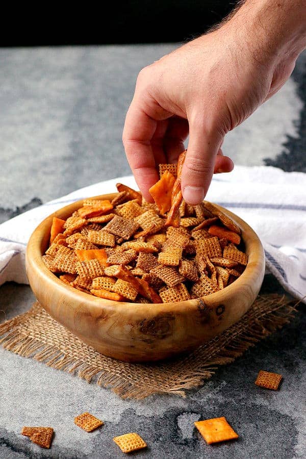Hand grabbing chex mix out of a wooden bowl