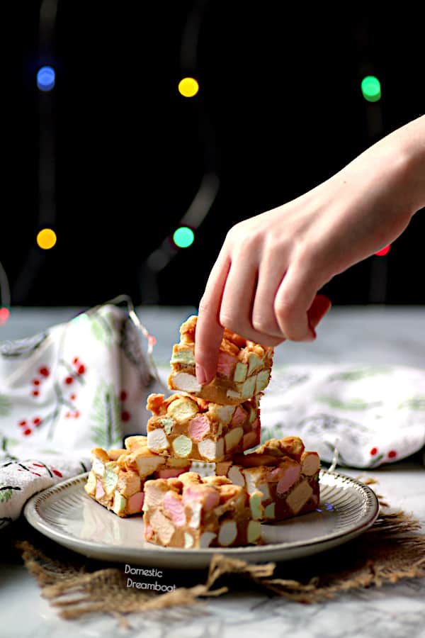 Hand grabbing a Peanut Butter Butterscotch Confetti Squares from a plate