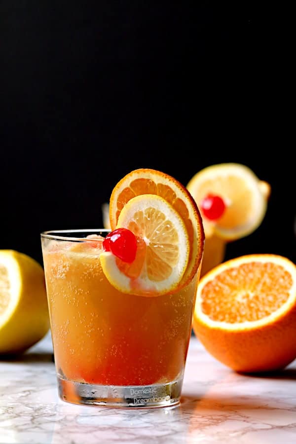 A glass of brandy slush cocktail garnished with citrus slices and a cherry.