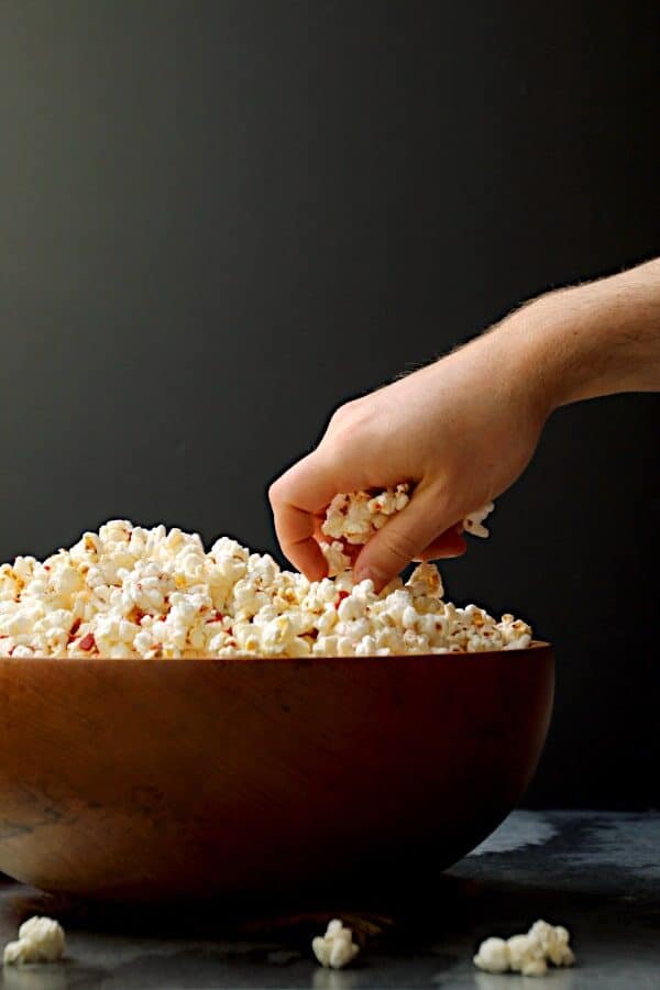 A hand grabbing a handful of popcorn from a large wooden bowl.