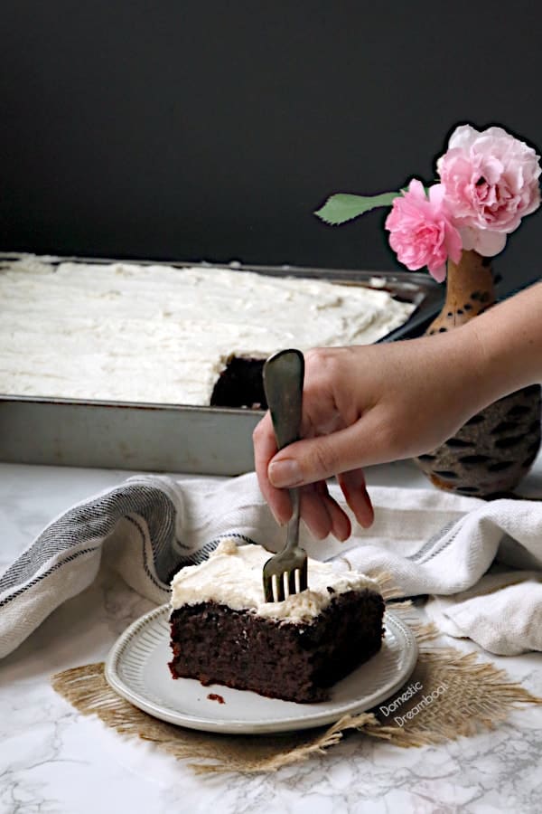 A hand sticking a fork into a slice of chocolate zucchini cake