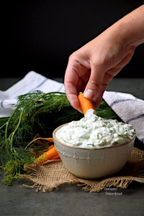 A hand dipping a carrot in a bowl of tzatziki