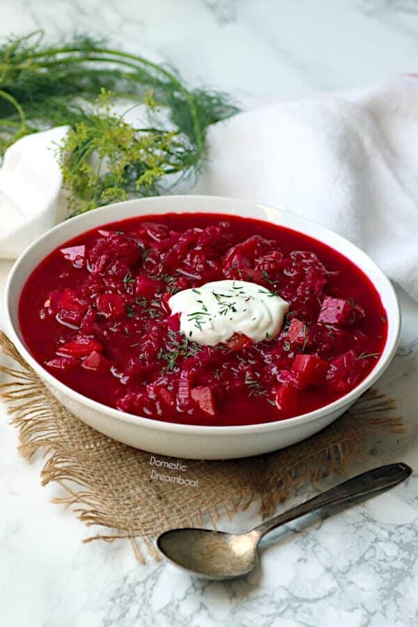 Beet borscht in a white bowl garnished with fresh dill and sour cream.