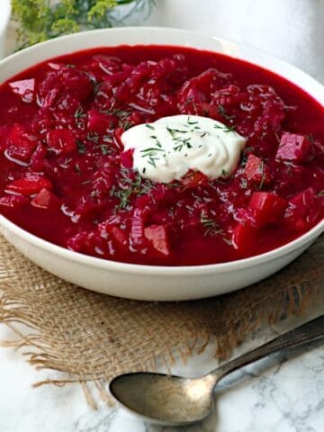 Beet borscht in a white bowl garnished with fresh dill and sour cream.