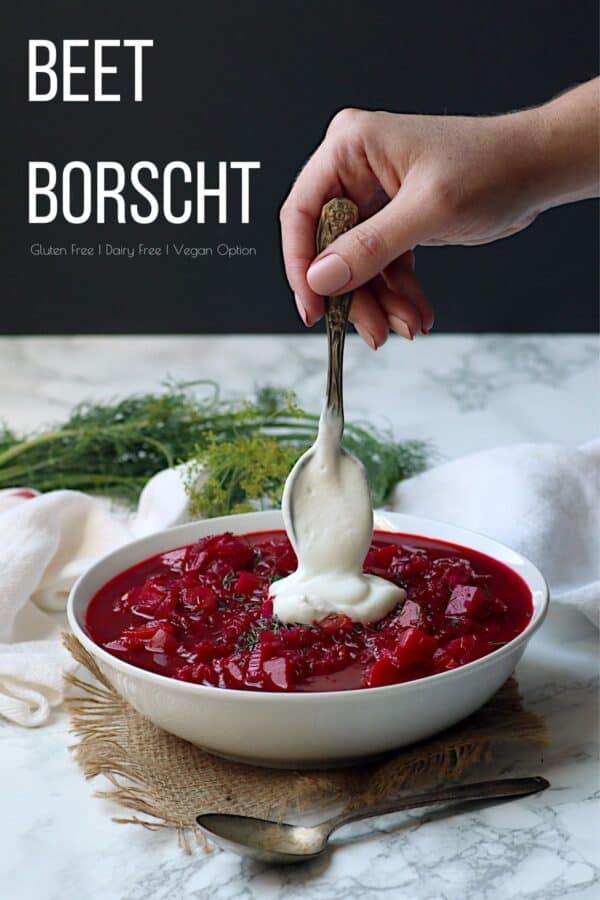 A hand adding a dollop of sour cream to a bowl of beet borscht.