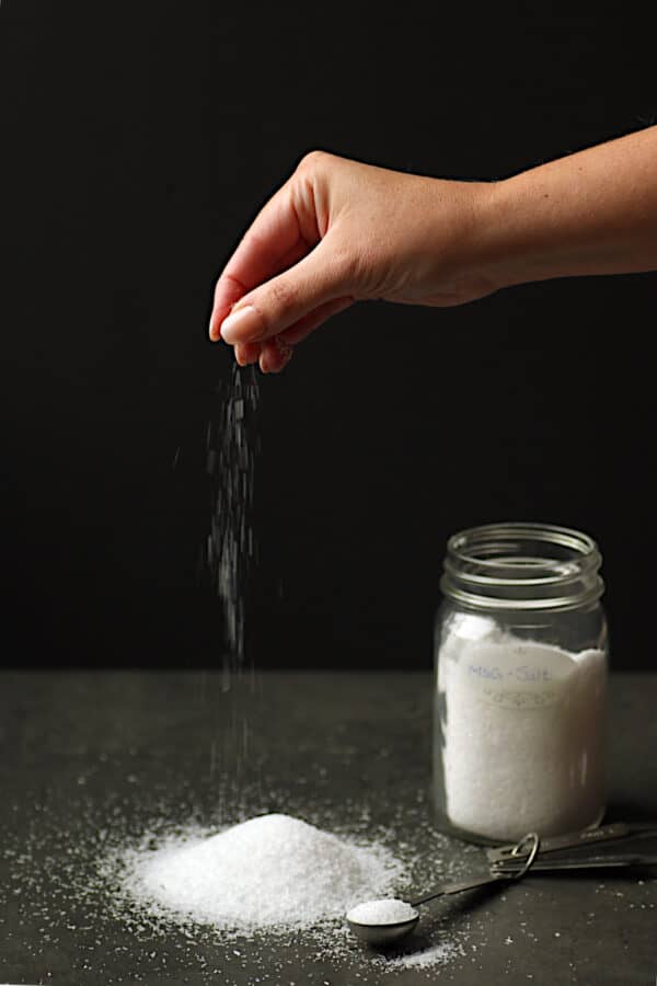 A hand sprinkling a mixture of MSG and salt