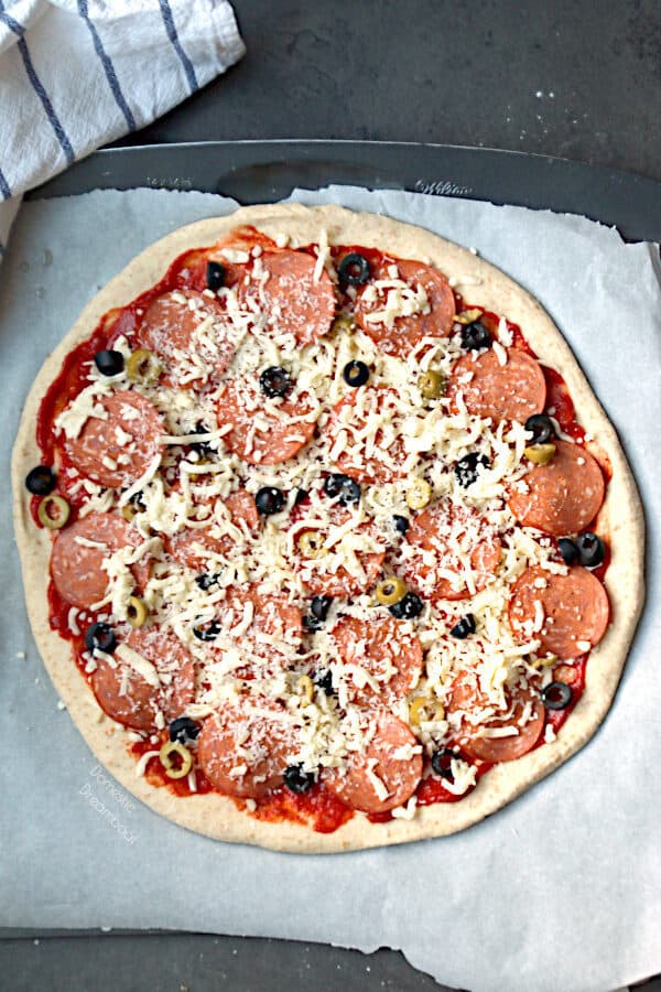 An uncooked homemade pizza with pepperoni and olives.