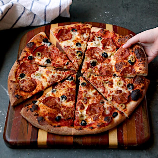 A hand grabbing a slice of homemade pizza.