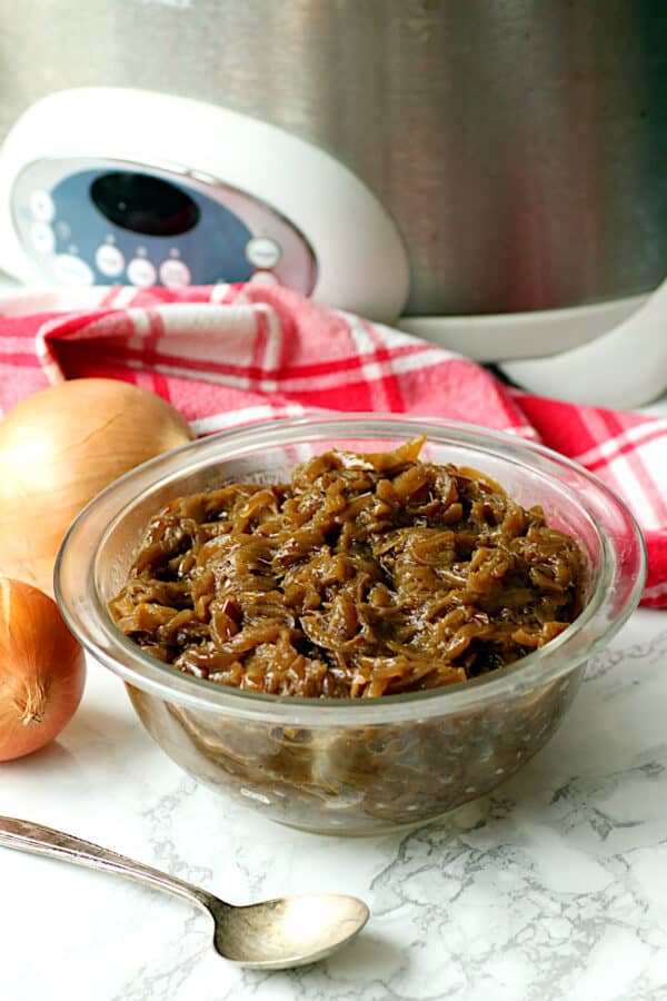 Caramelizes onions in a clear glass bowl with a slow cooker in the background.