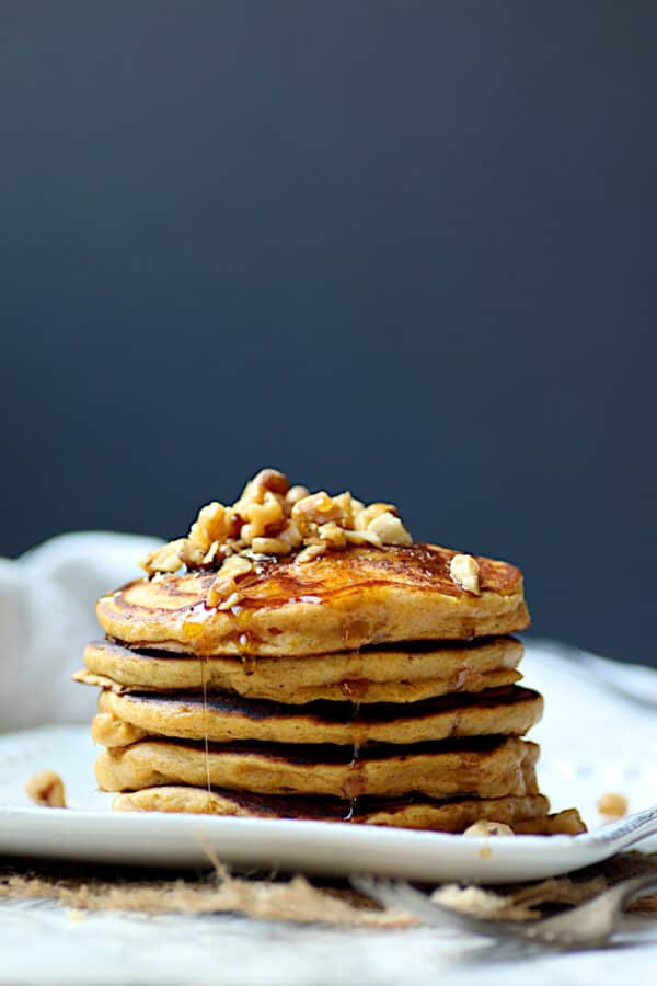 A stack of pumpkin spice pancakes garnished with chopped walnuts and maple syrup.