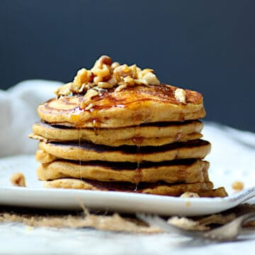 A stack of pumpkin spice pancakes garnished with chopped walnuts and maple syrup.