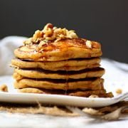 A stack of pumpkin spice pancakes with chopped pecans and syrup.
