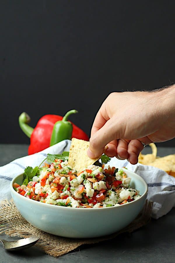 A hand dipping a tortilla chip in a bowl of ceviche
