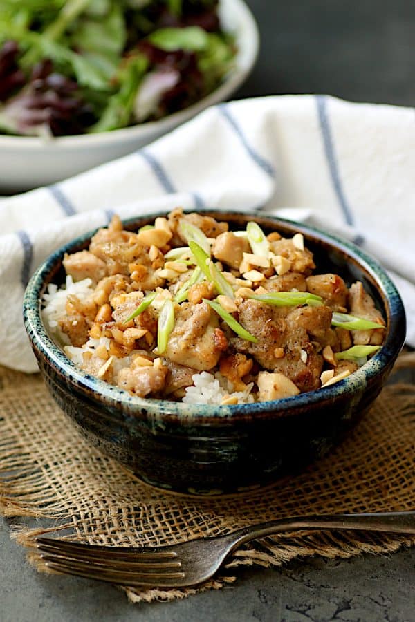 Ginger peanut chicken over rice in a blue, pottery bowl.