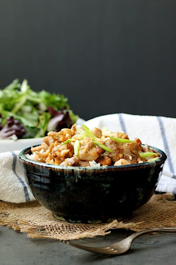 Ginger peanut chicken over rice in a blue, pottery bowl.