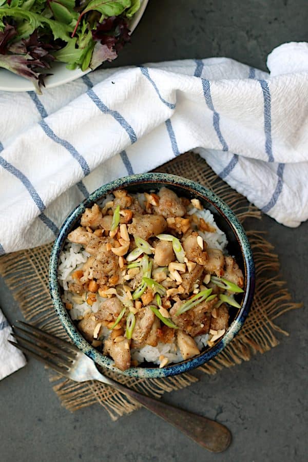 An overhead photo of ginger peanut chicken over rice in a blue, pottery bowl.