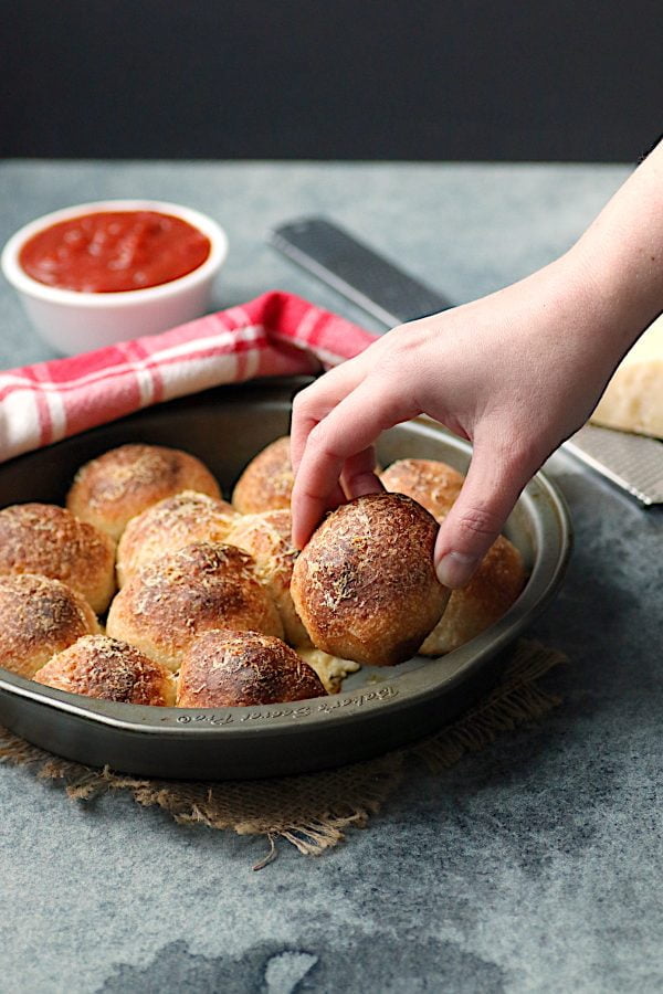A hand grabbing a pizza roll from a round baking pan.