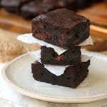 A stack of fudgy brownies on a white plate.