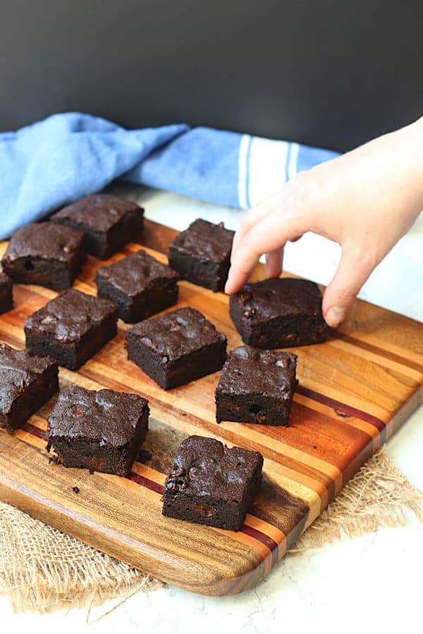 A hand grabbing a brownie from a wooden cutting board.