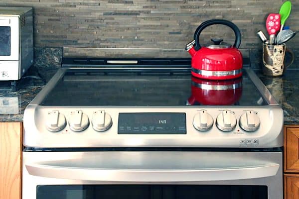 A stainless steel induction range with a red kettle on top.