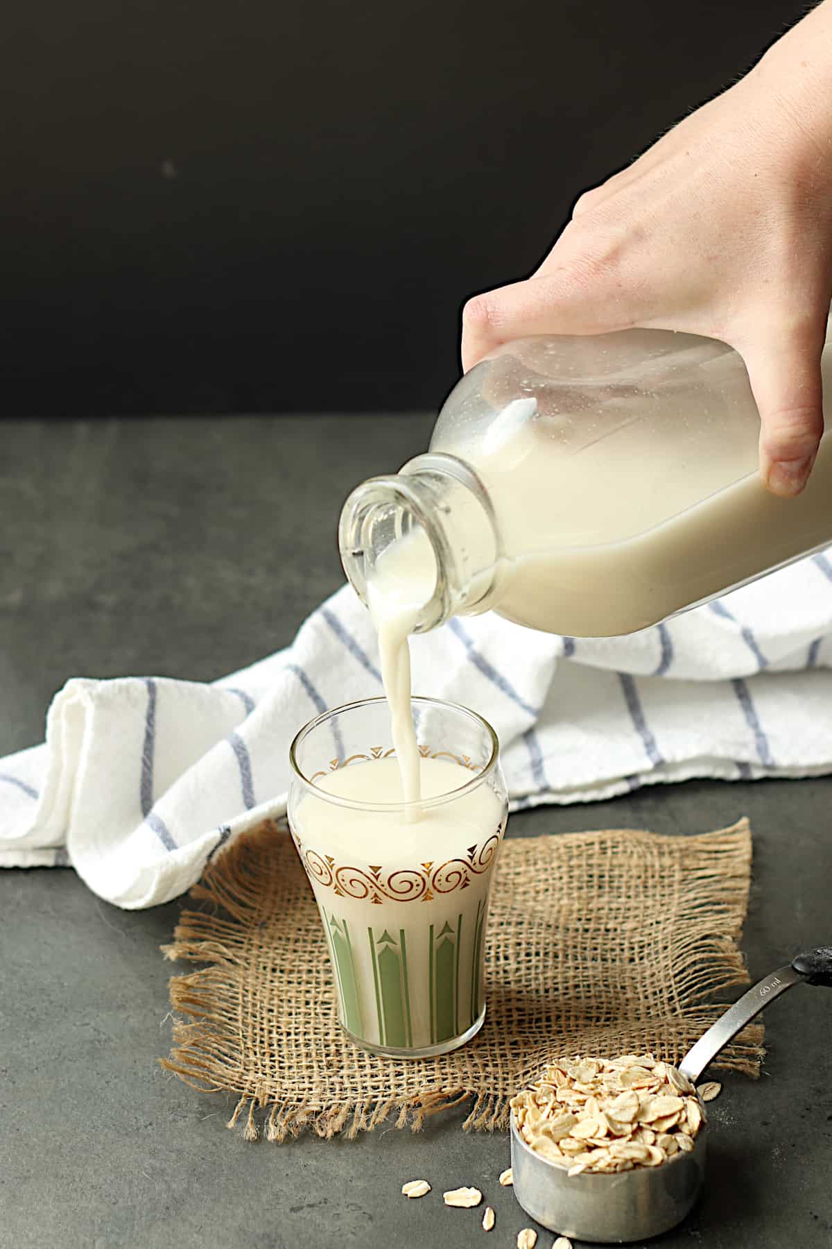 A hand pouring homemade oat milk from a glass bottle into a glass