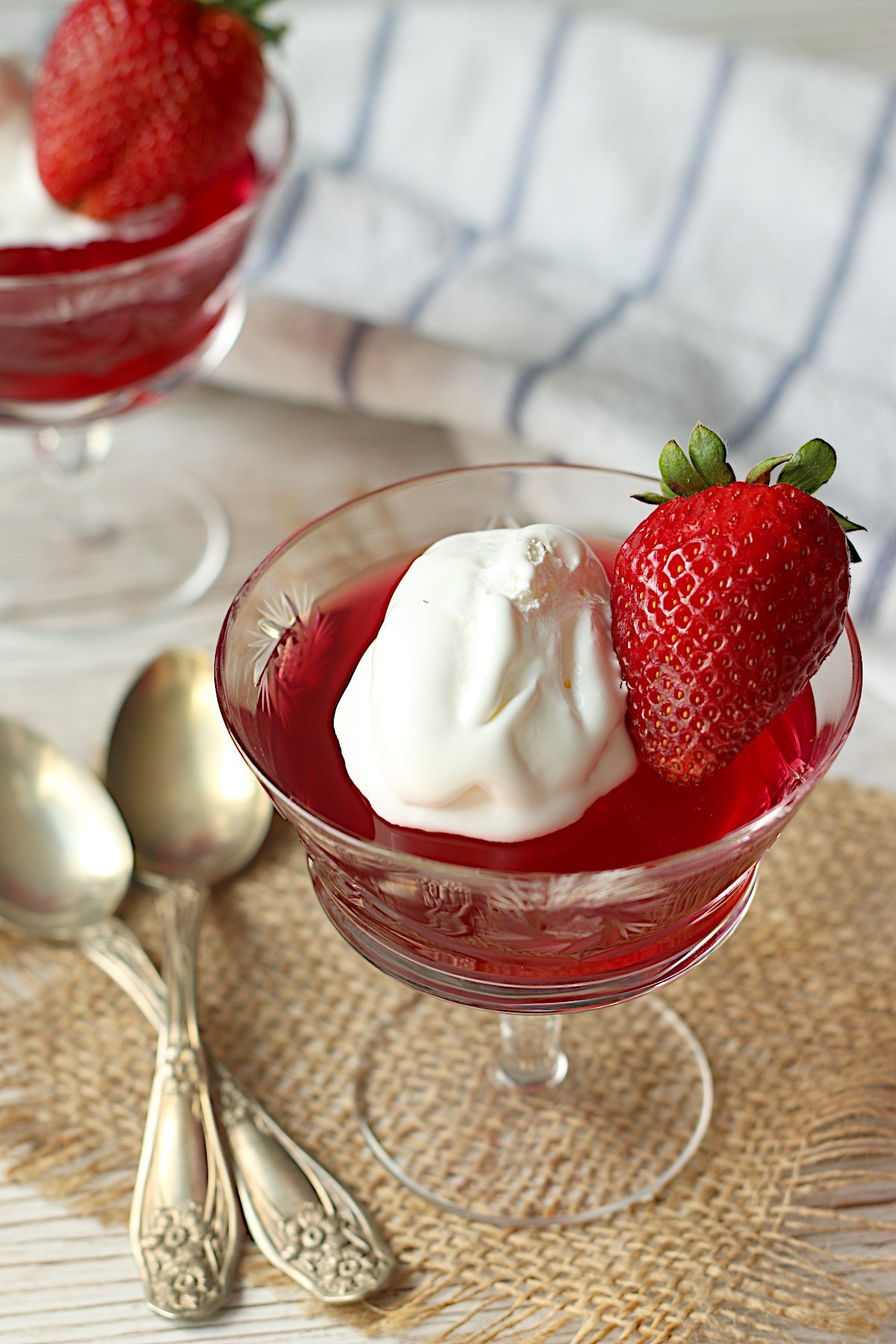 Homemade jello in a crystal glass, garnished with whipped topping and a fresh strawberry.