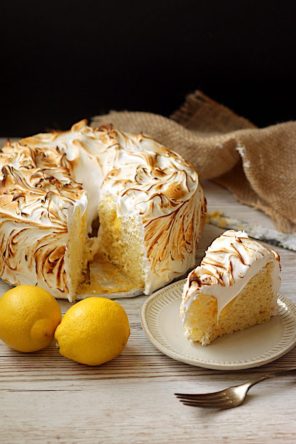 A slice of homemade lemon meringue chiffon cake on a plate, with the whole cake in the background.