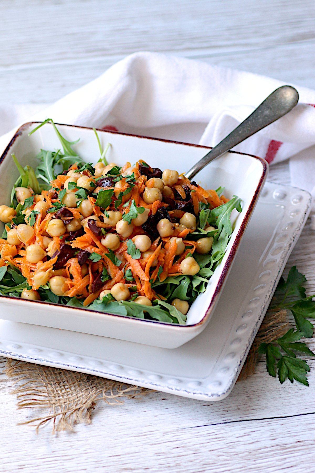 Chickpea salad with carrots and olives in a square, white bowl.