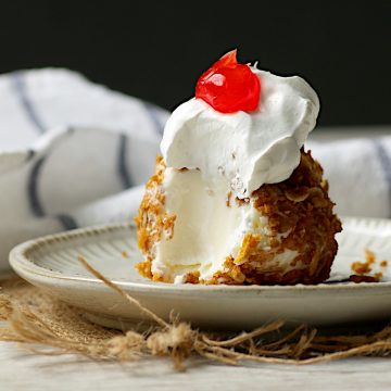 Homemade no fry deep fried ice cream topped with whipped cream and a cherry, with a spoonful removed.
