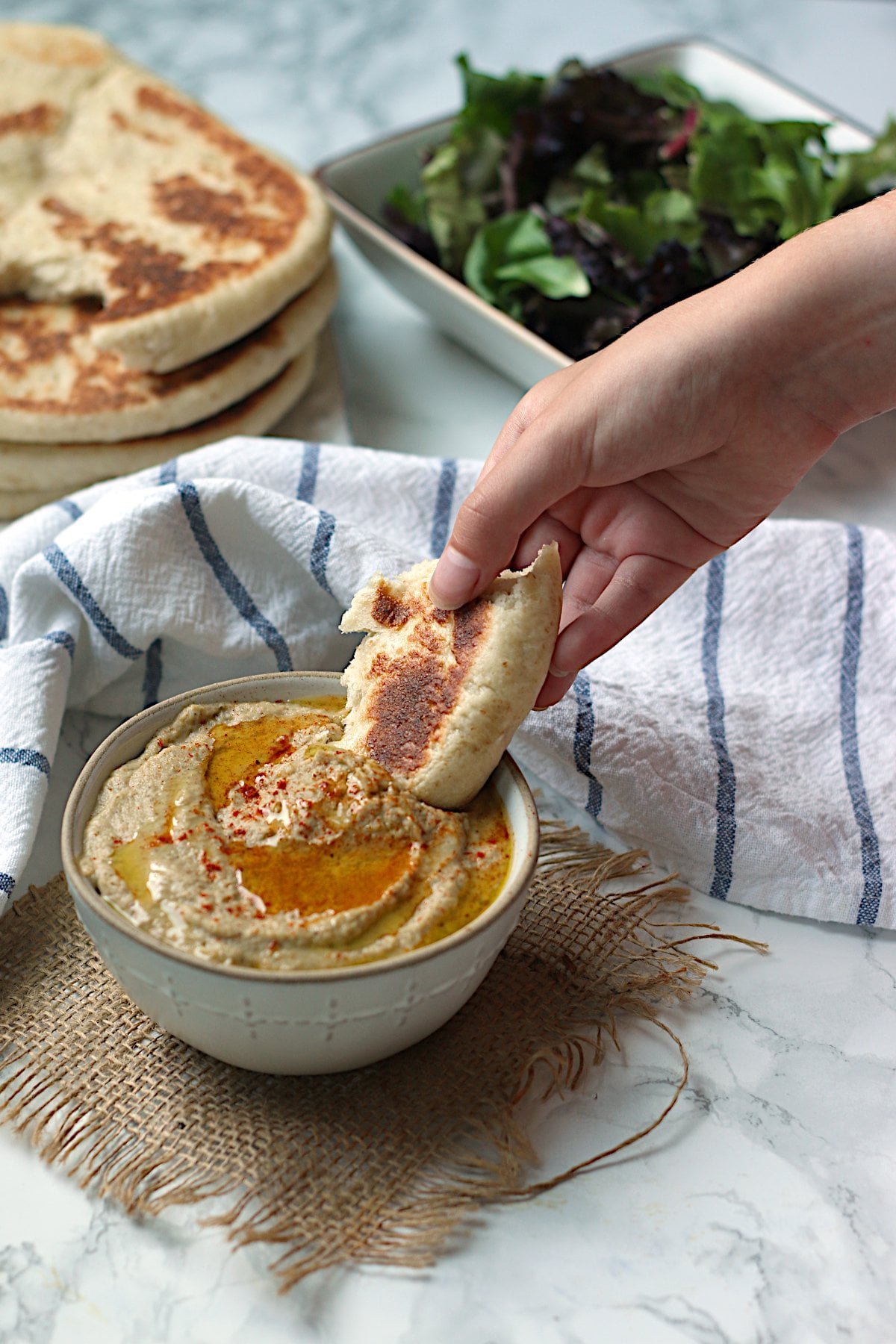 A hand dipping a piece of flatbread into a bowl of baba ghanouj.