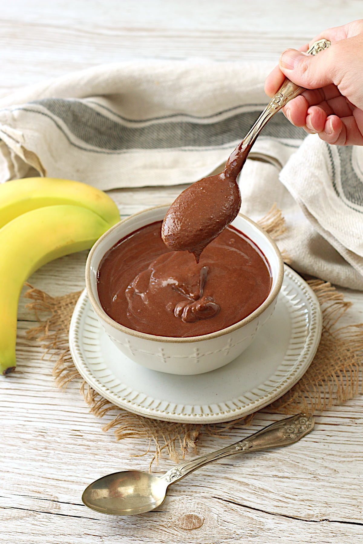 A spoonful of vegan chocolate banana pudding being scooped from a white bowl.