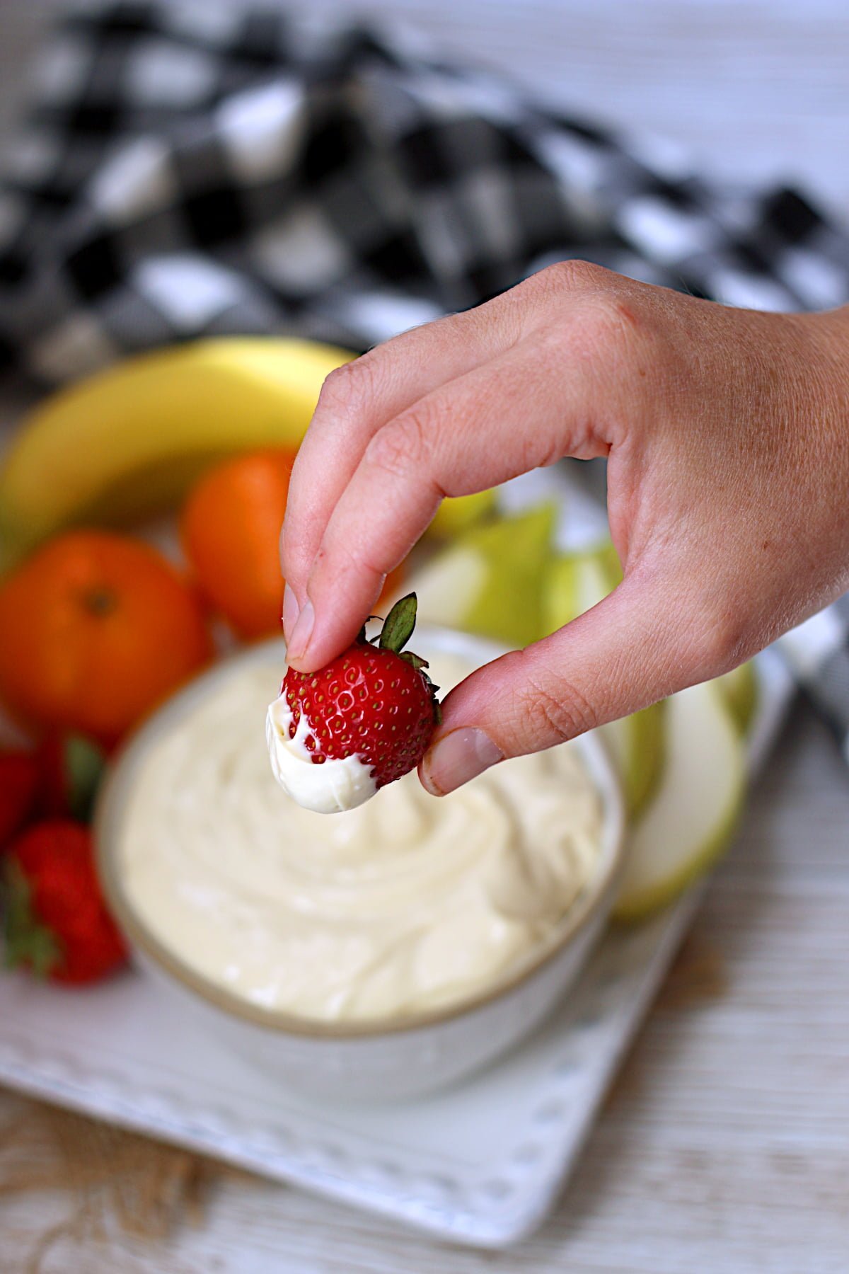 A hand holding a strawberry dipped in orange dream fruit dip.
