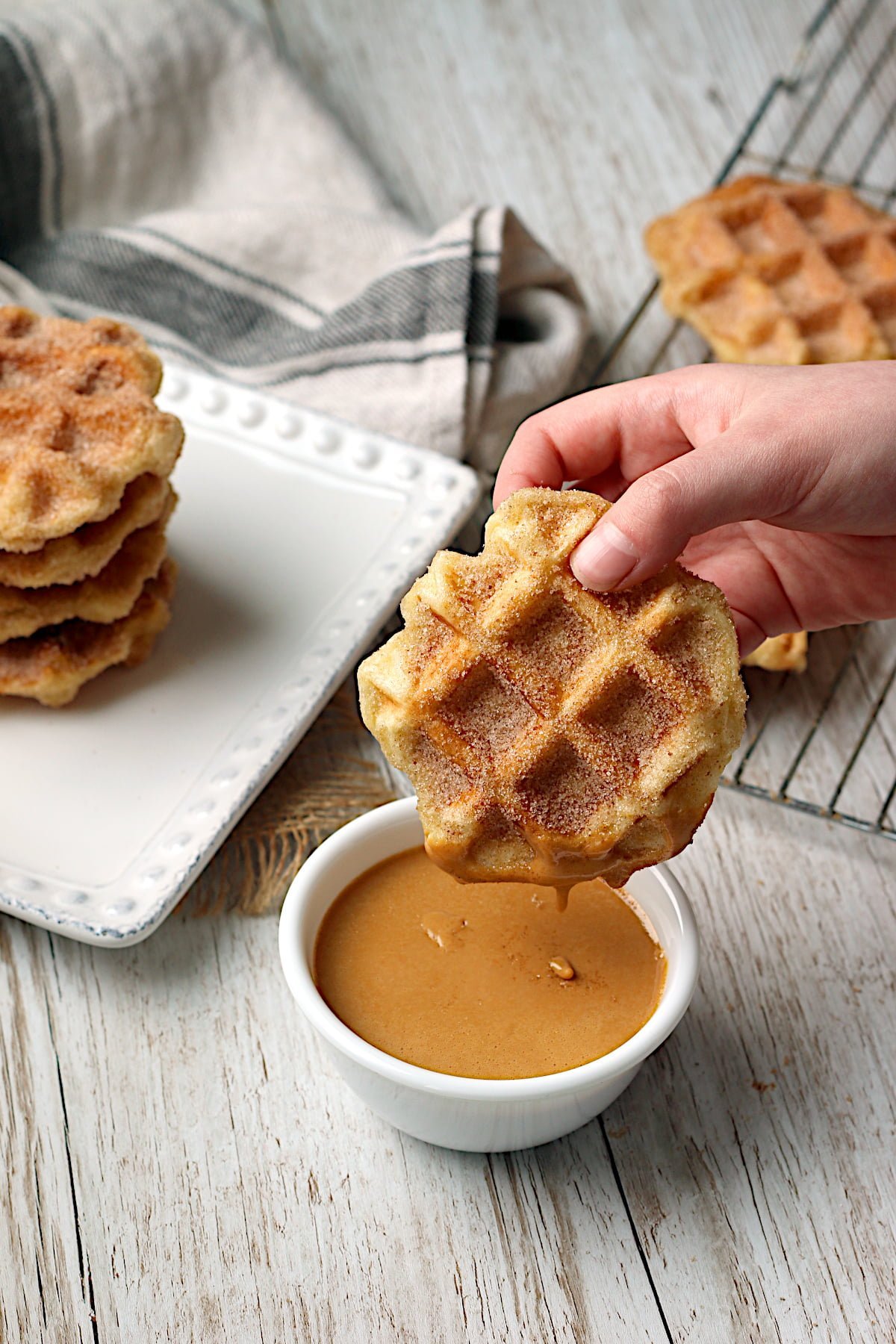 A hand dipping a homemade Churro Waffle into a small bowl of dulce de leche