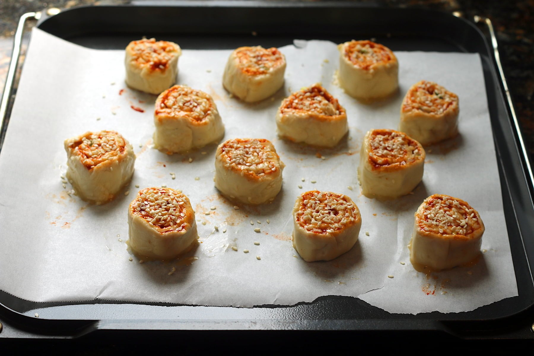 Gochujang cheddar pinwheels on a baking sheet before baking.
