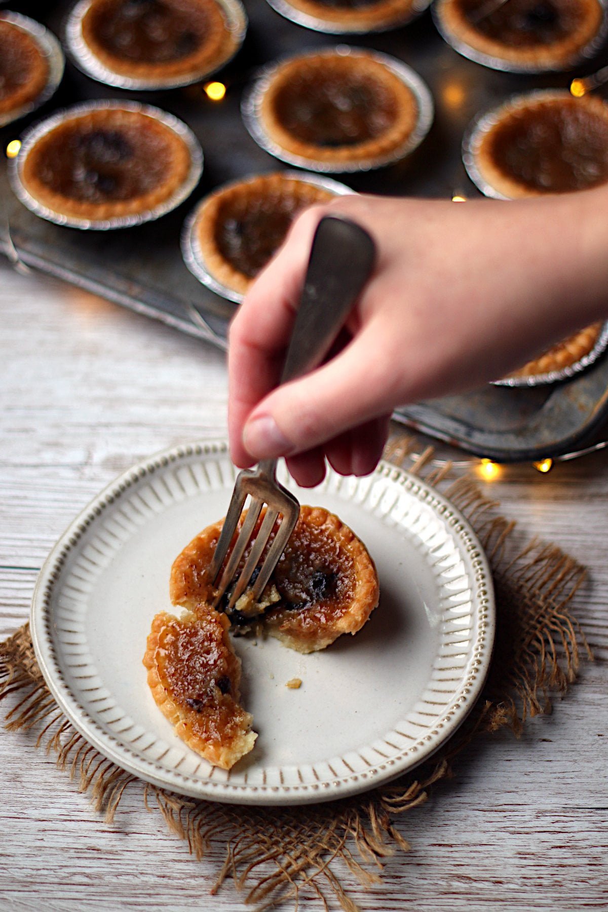 A fork breaking a butter tart with raisins in half on a small white plate.