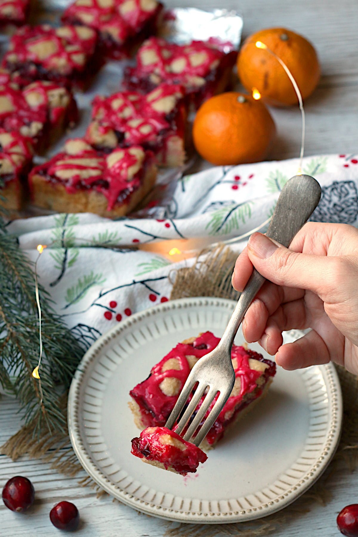 A fork picking up a piece of cranberry pie bar from a small white plate.