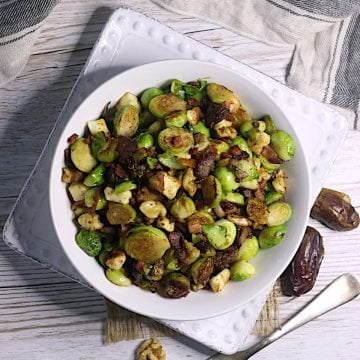 Overhead photo of Brussels Sprouts with Bacon, Halloumi, and Dates in a white bowl.