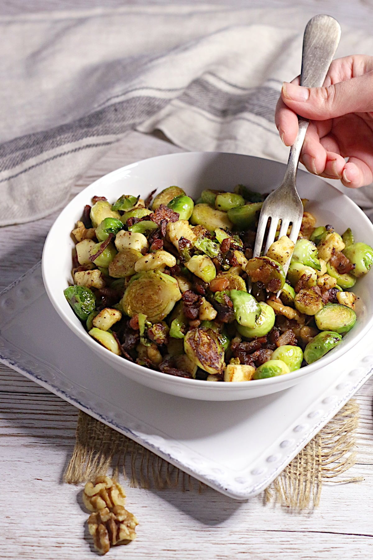 A fork scooping from a white bowl full of Brussels Sprouts with Bacon, Halloumi, and Dates.
