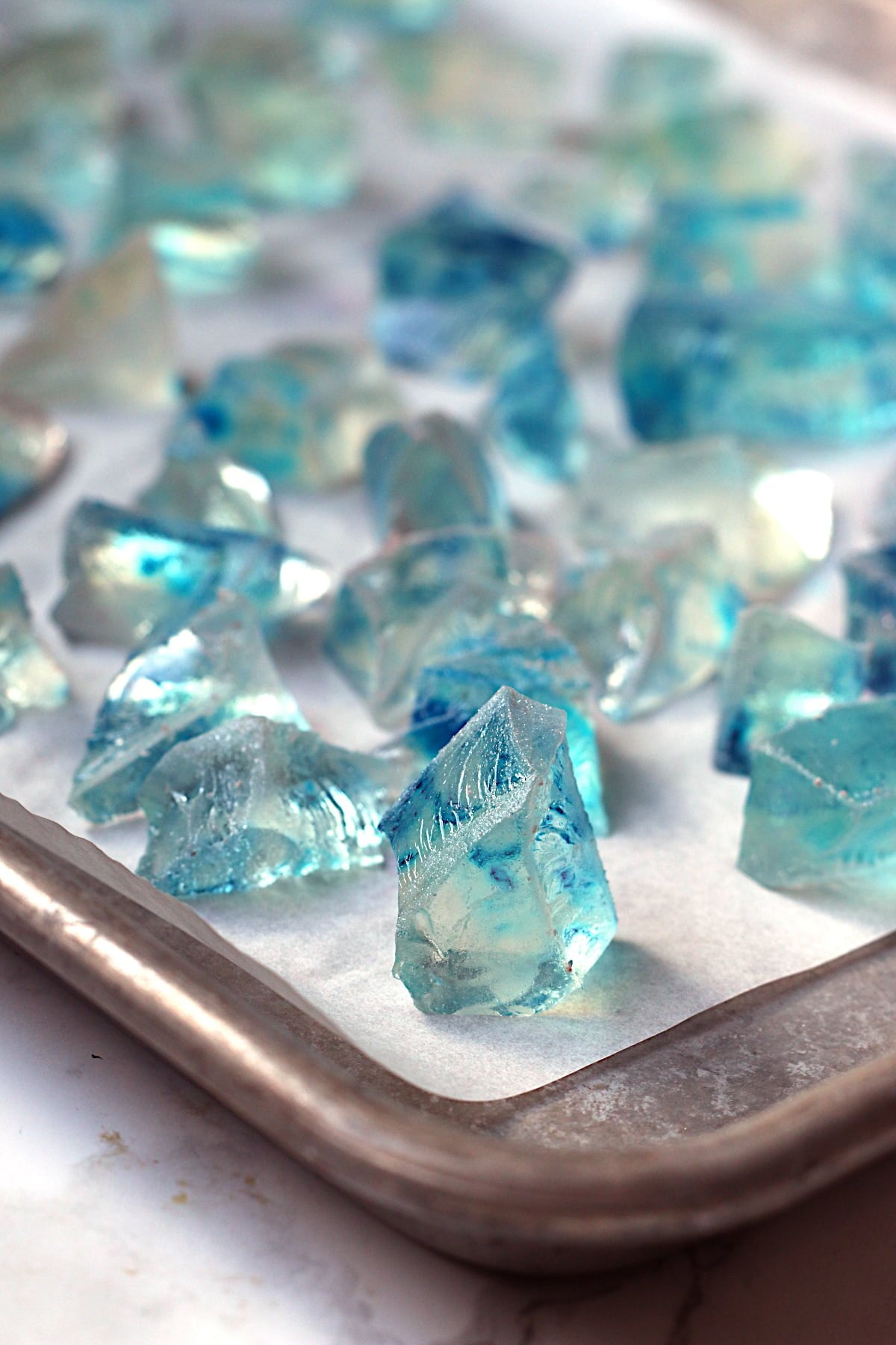 A closeup photo of blue Japanese Crystal Candy on a parchment-lined baking sheet.