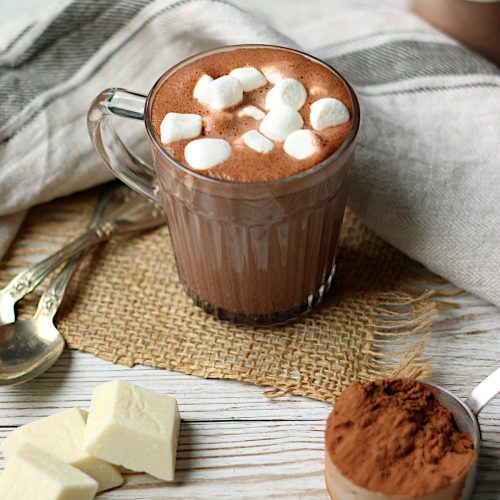 Homemade hot chocolate with mini marshmallows in a clear glass mug.
